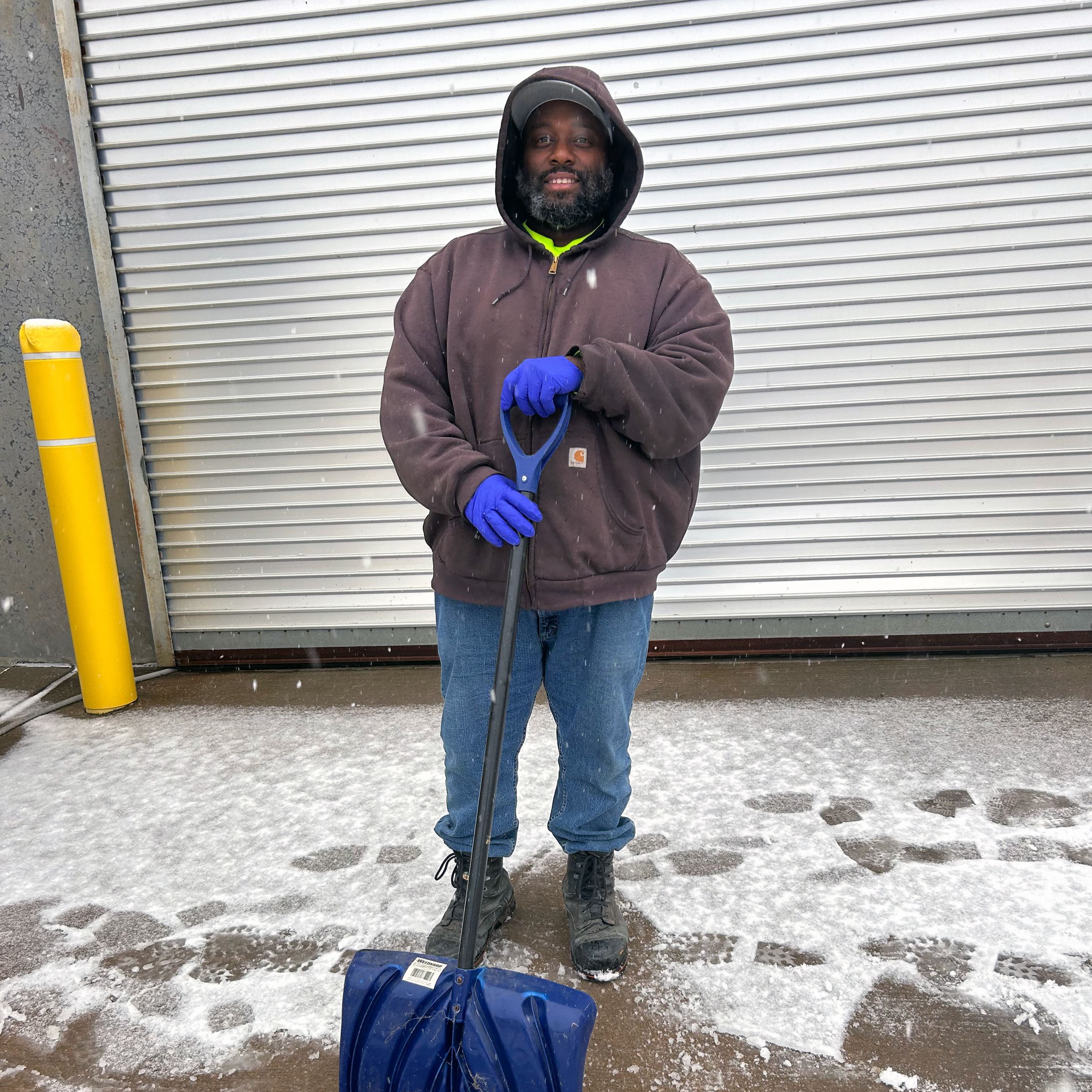 A man in a hooded sweatshirt poses with a snow shovel.