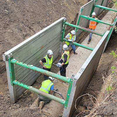 Workers are in a deep hole that is reinforced by metal walls. They are repairing a water pipeline.
